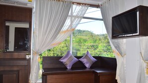 A room with a large window, a wooden bench with cushions, a television mounted on the wall, and a small table with a plant. - Lanta Nice Beach House (Ko Lanta)