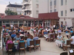 An outdoor dining area with multiple tables and chairs, surrounded by buildings. - Acropol Beach Hotel (Konyaalti)