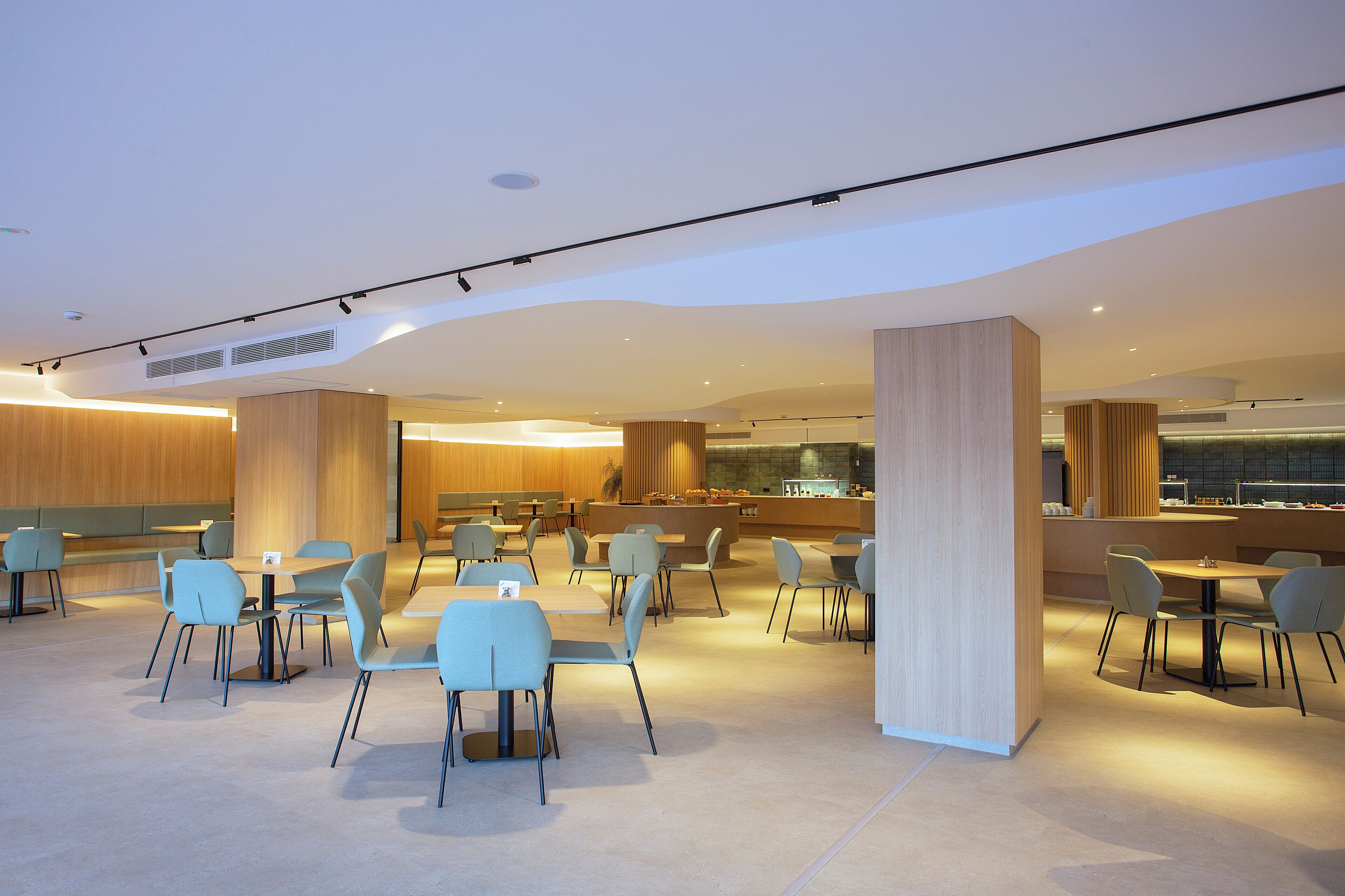 Un comedor amplio y moderno con varias mesas y sillas, una barra central y un gran pilar de madera.