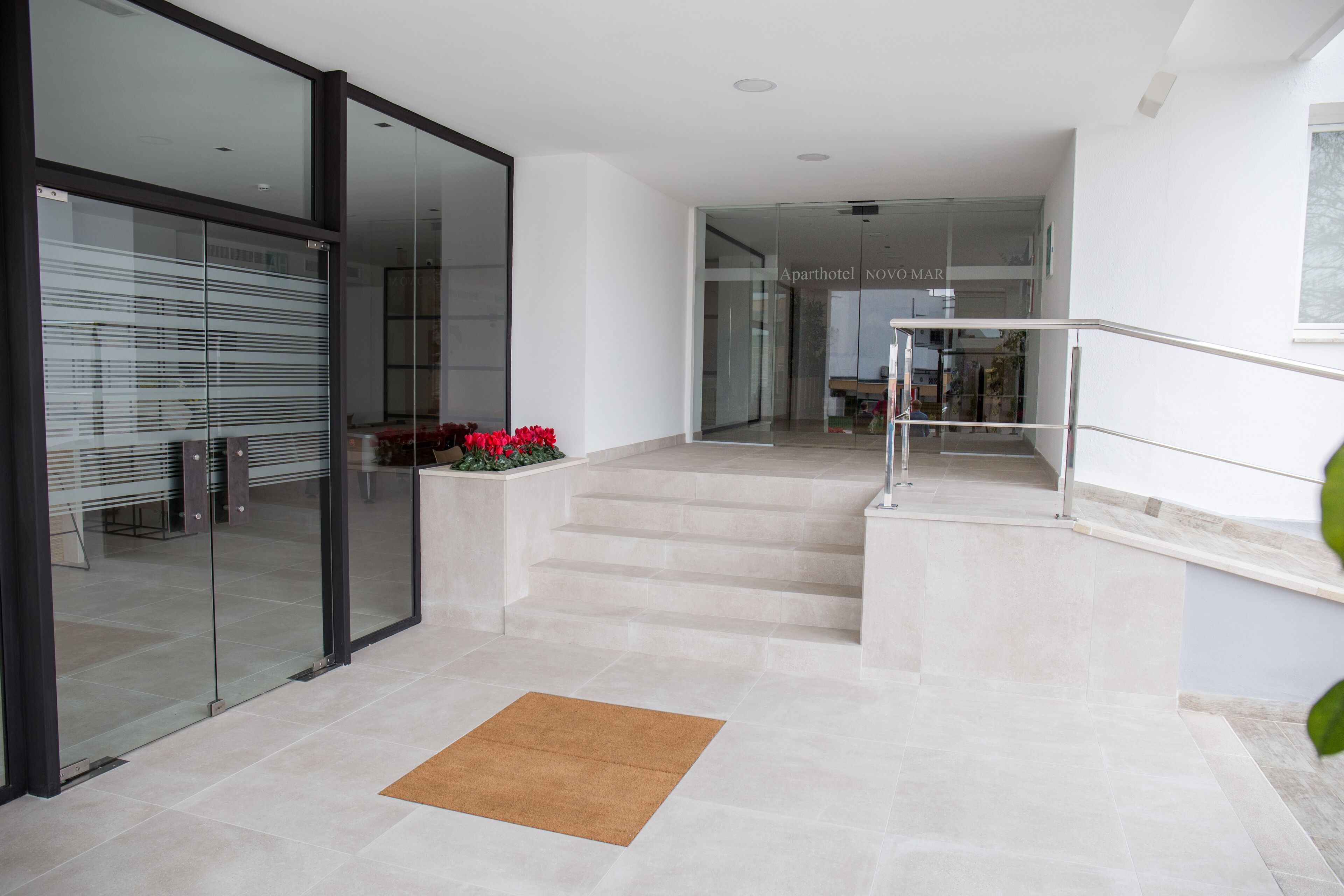 A modern hotel lobby with a glass door entrance, a staircase leading to an upper floor, and a reception area in the background.