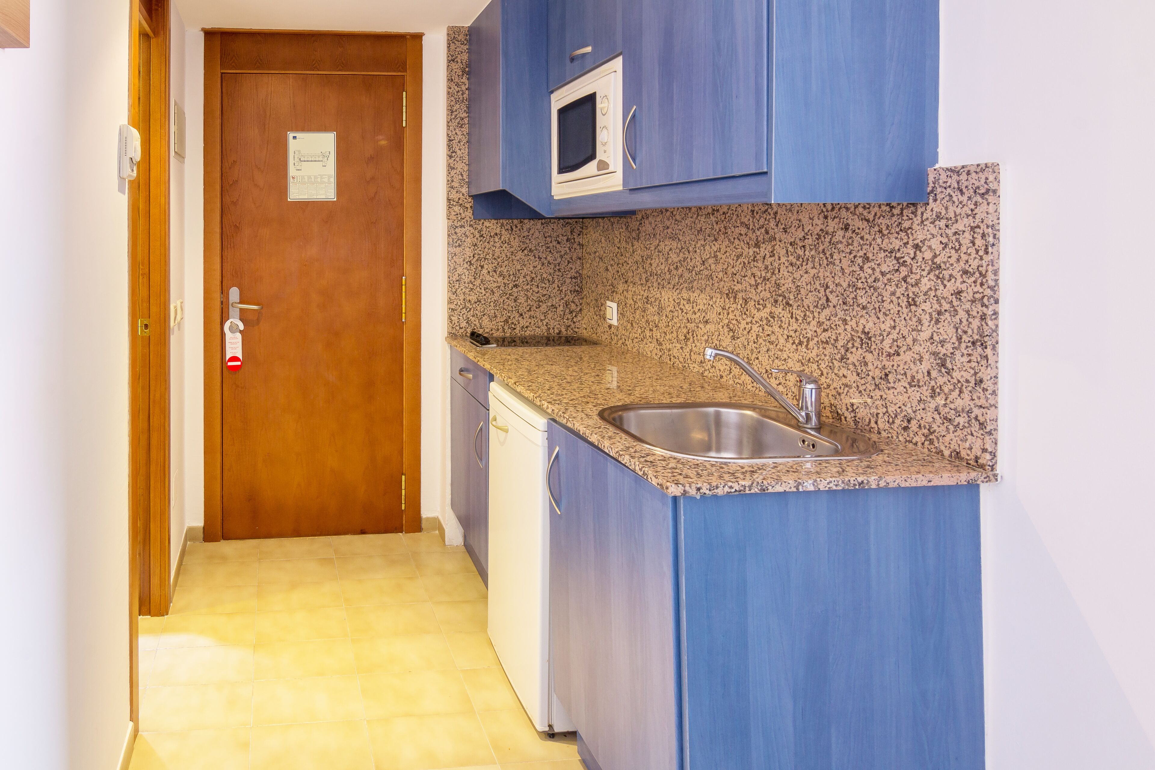 A compact kitchen with a granite countertop, stainless steel sink, and a microwave.