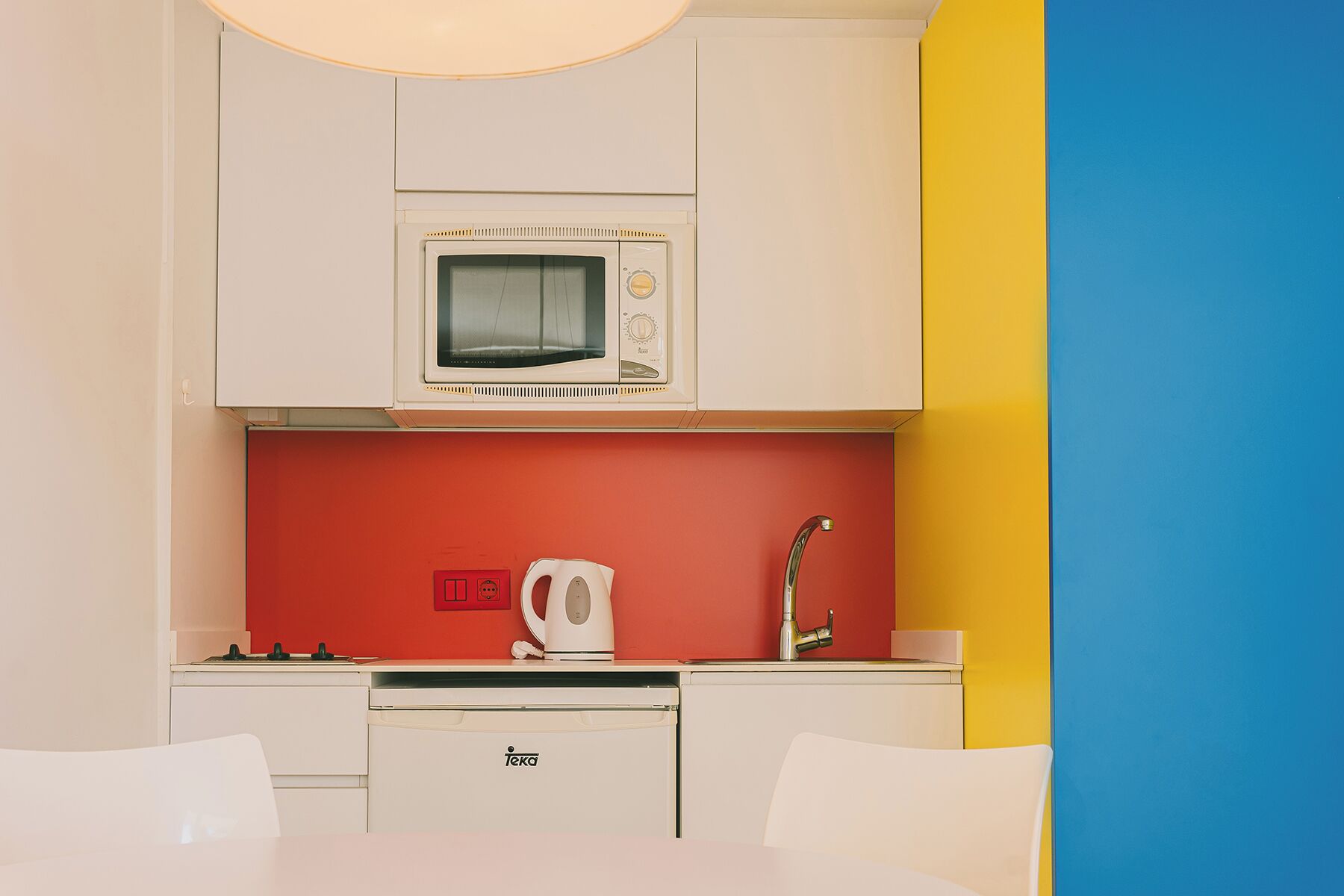 A compact kitchenette with a microwave, kettle, and sink.