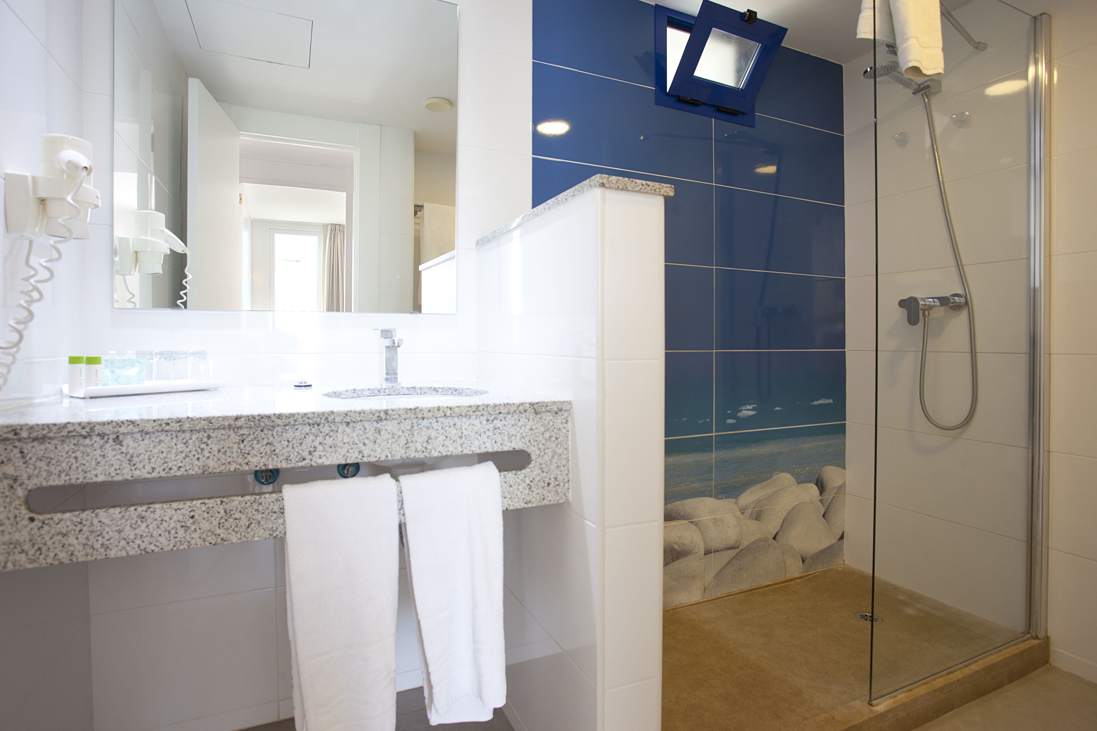 A modern bathroom with a granite countertop, a glass shower enclosure, and a visible door leading to another room.