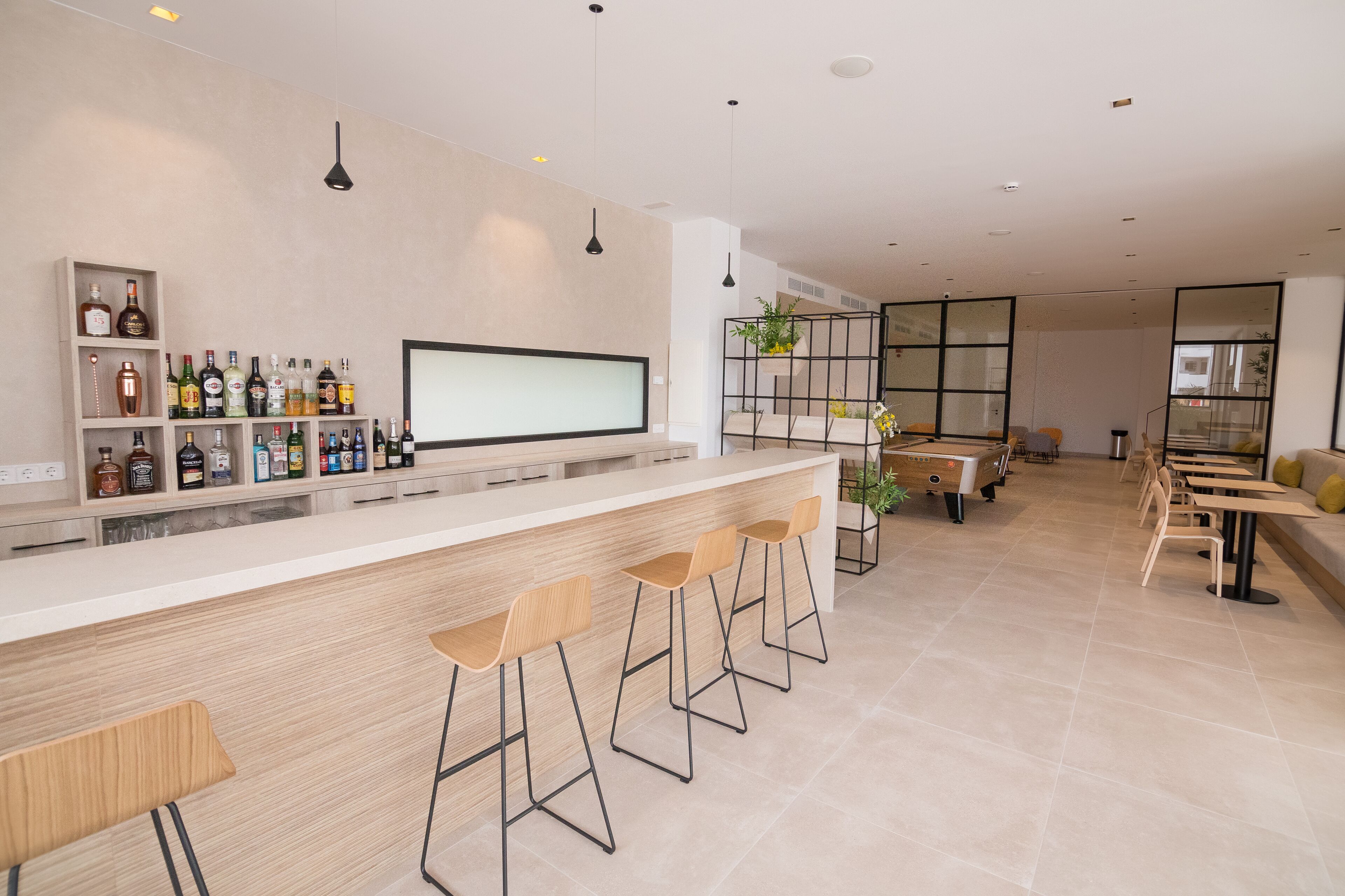 A modern bar area with a long counter, multiple stools, and shelves of bottles.