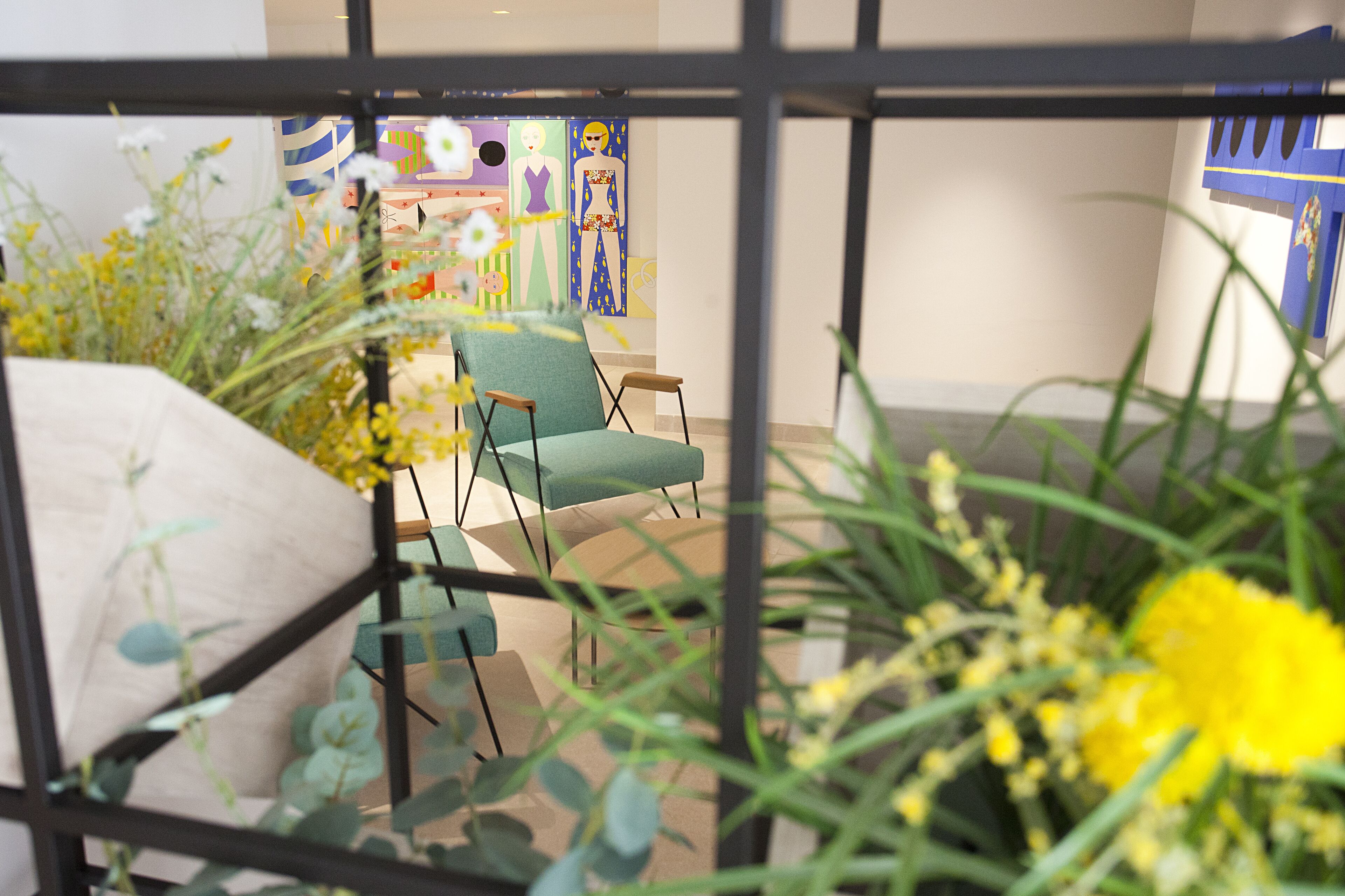 Ein Zimmer mit zwei grünen Stühlen, einem weißen Sofa und einer großen Kübelpflanze mit gelben Blüten.