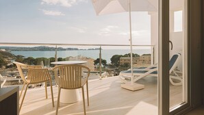 A balcony with a table and chairs, a white umbrella, and a view of the sea and buildings. - Aparthotel Novo Mar (Calvia)
