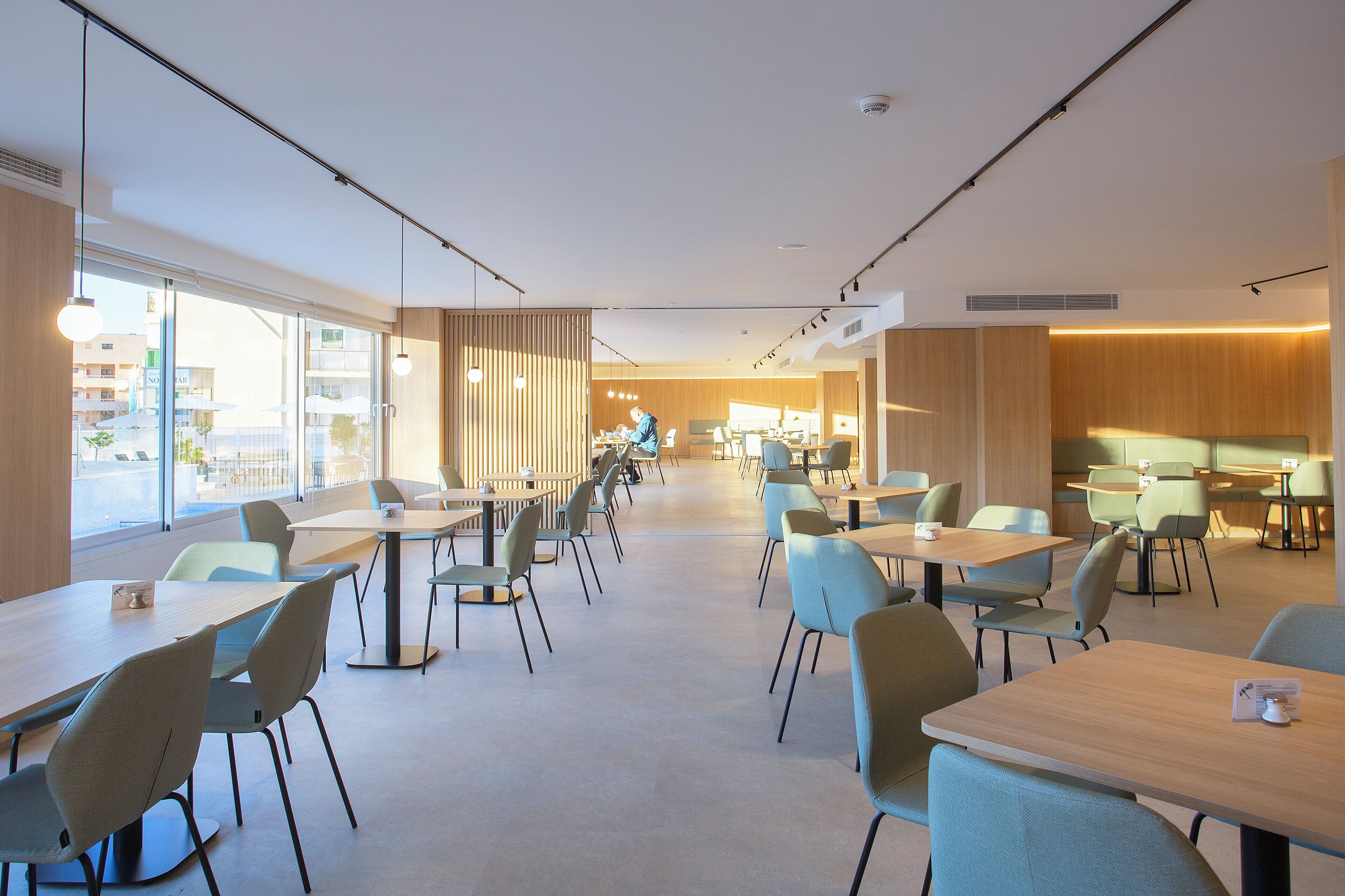 A modern dining area with long tables and chairs, large windows, and a view of the city.