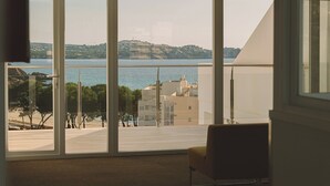 A room with large floor-to-ceiling windows offering a view of a coastal area with buildings and a hill in the distance. - Aparthotel Novo Mar (Calvia)