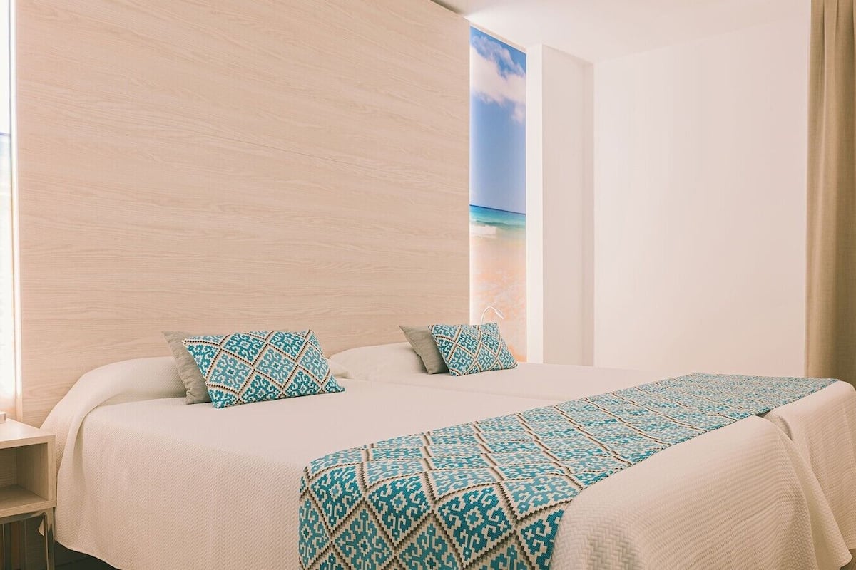 Habitación de hotel con cama, almohadas, mesita de noche y un cuadro en la pared.