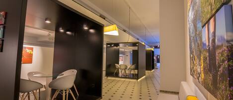 A modern hotel corridor with a checkered floor, a seating area with white chairs, and a large wall mural.