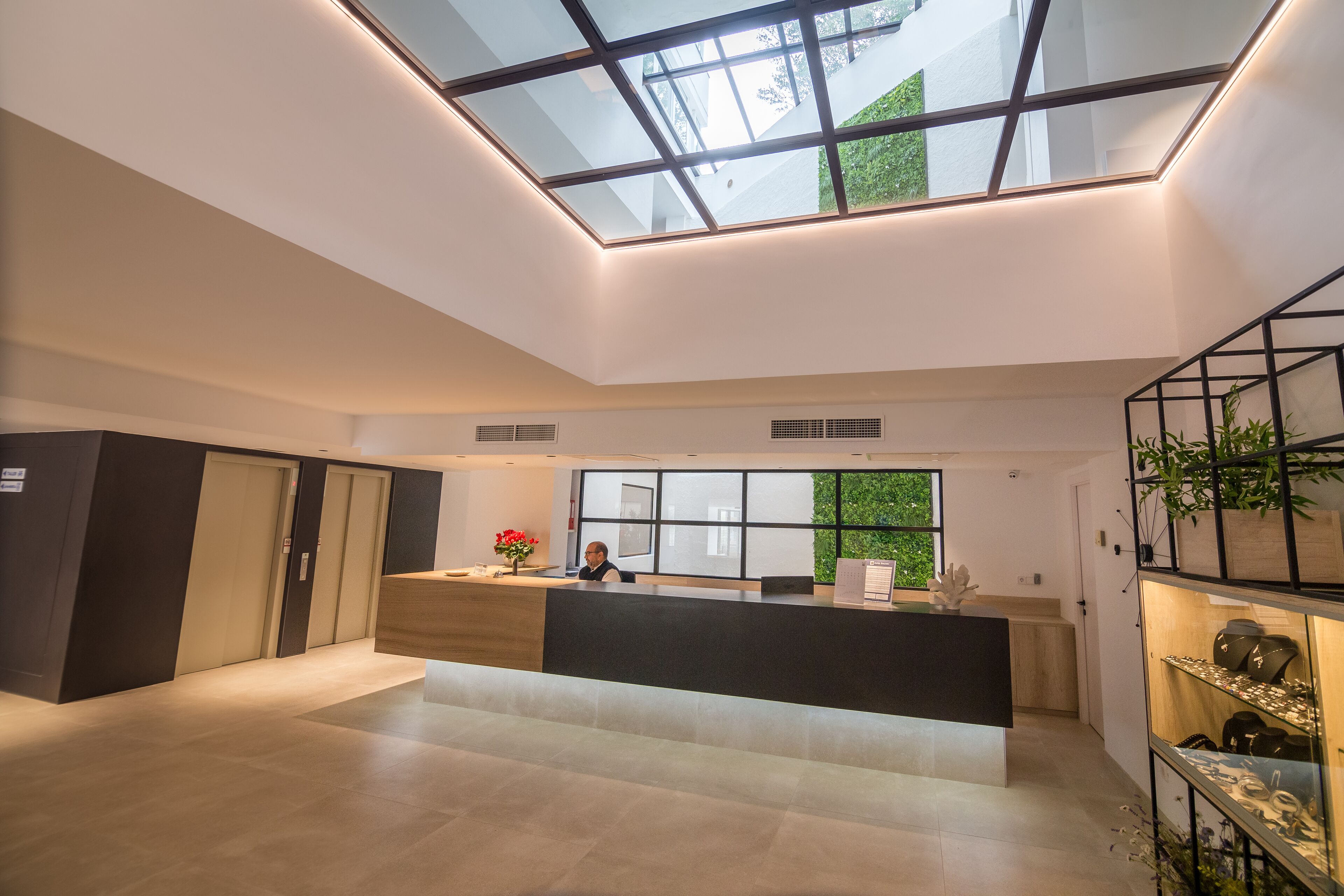 A modern reception area with a skylight, a reception desk, a plant display, and a view of greenery outside.