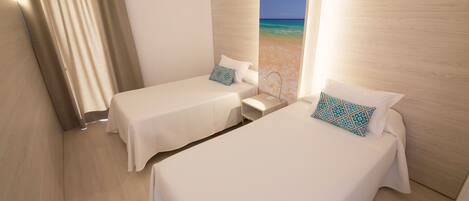 Habitación de hotel con dos camas, una mesita de noche y vista a la playa.