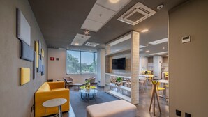 A modern hotel lobby with a seating area, a television, and a view of the outdoors. - City Express Plus by Marriott Guadalajara Palomar (Tlajomulco de Zúñiga)