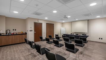 Un salón de conferencias con una pizarra, proyector y una larga mesa con sillas.