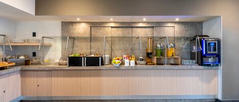 A modern breakfast bar with a coffee machine, fruit bowl, and various food items.