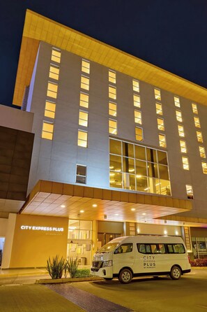 Ein modernes Hotelgebäude mit einem weißen Lieferwagen davor, beschriftet mit 'CITY EXPRESS PLUS BY MARRIOTT'.