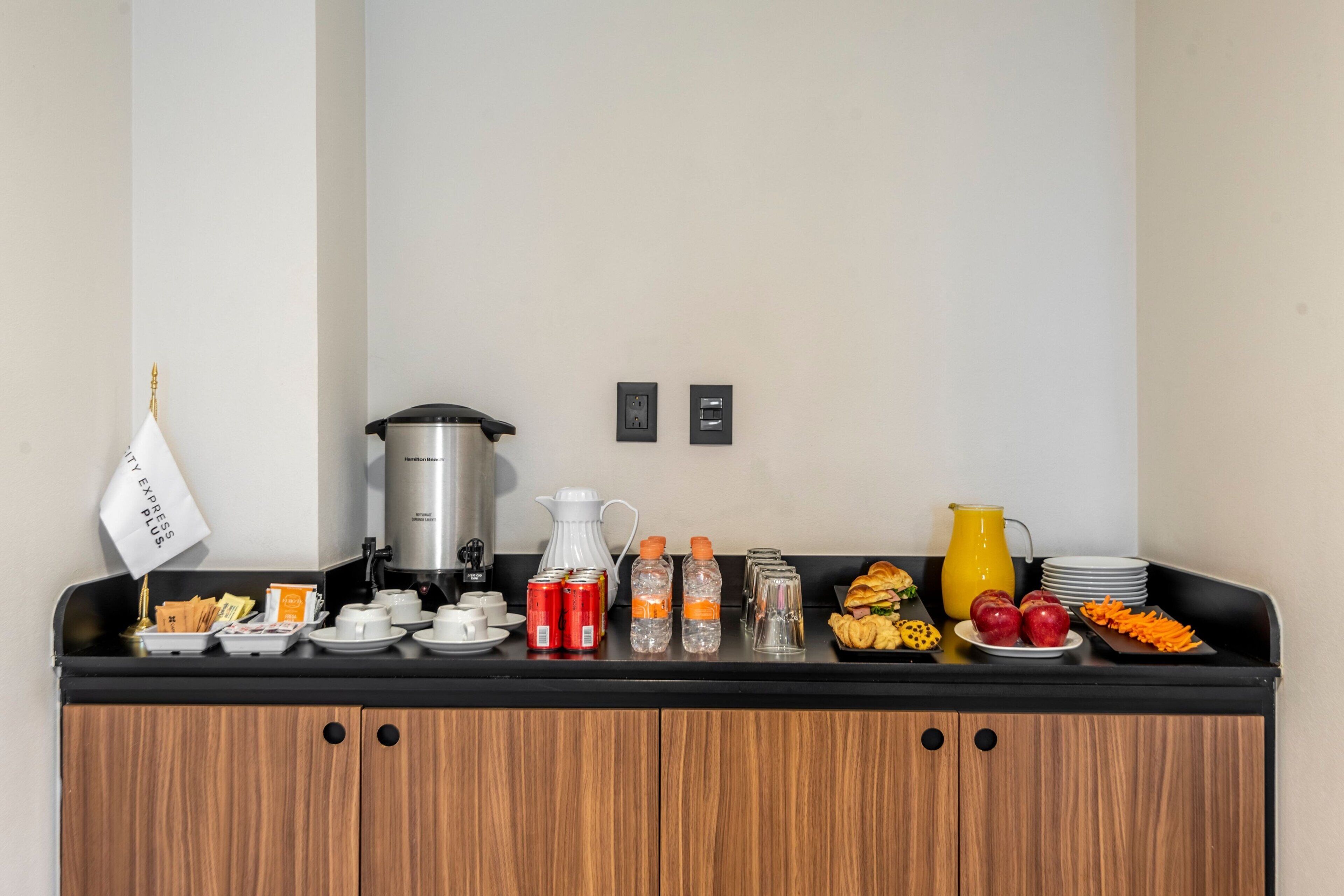 A breakfast bar with coffee makers, a kettle, and various food items like fruits and pastries.