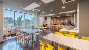A modern dining area with tables and chairs, large windows, and a kitchen area in the background. - City Express Plus by Marriott Guadalajara Palomar (Tlajomulco de Zúñiga)