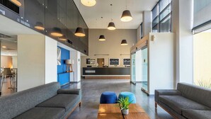 Un lobby moderno con sofás grises, una mesa de centro de madera con una planta e iluminación colgante.