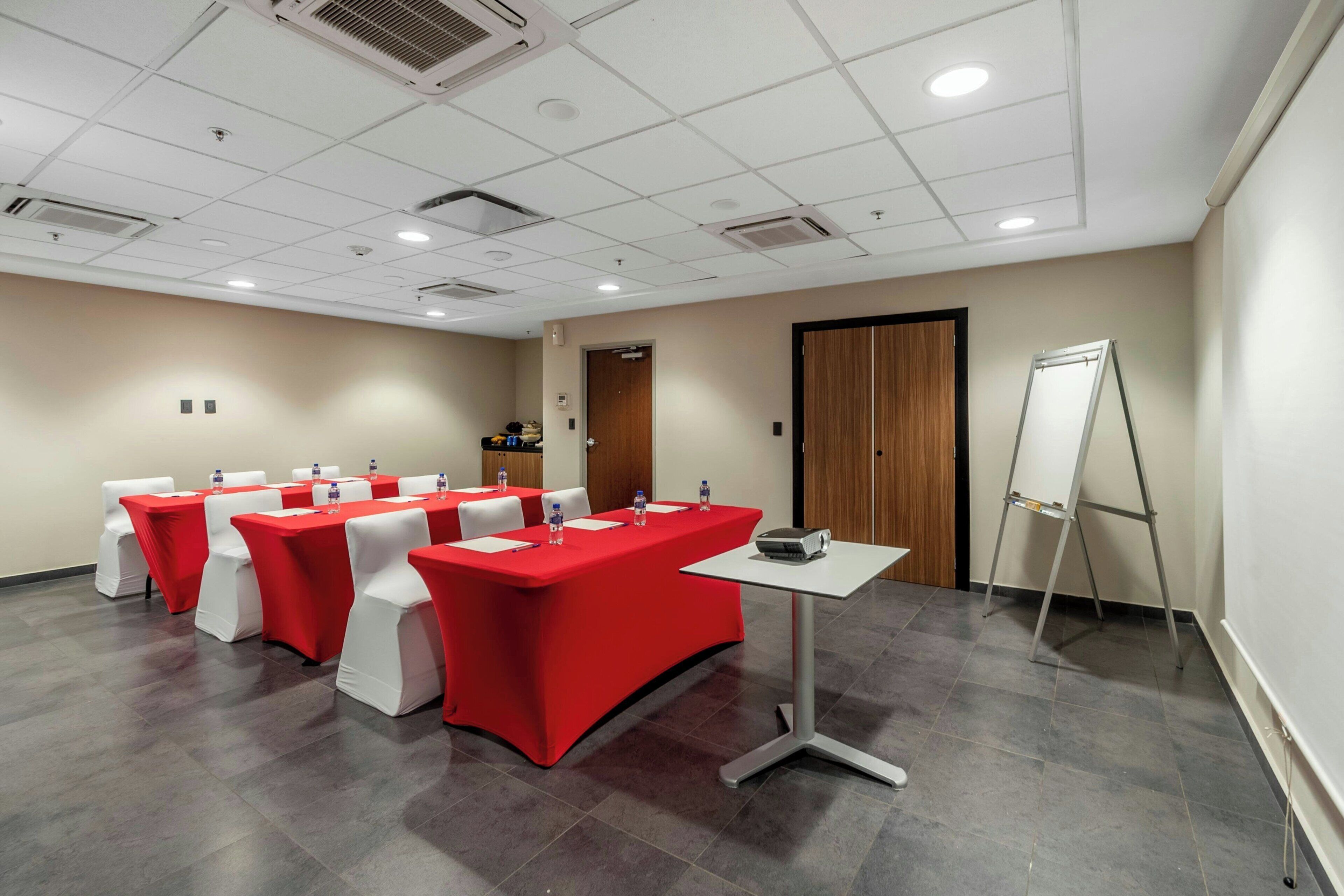 A conference room with red tables and white chairs, a projector, and a whiteboard.