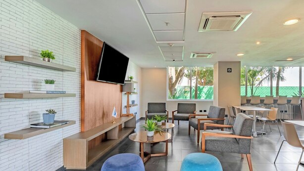 Un moderno vestíbulo de hotel con pared de ladrillo, mostrador de recepción de madera, zona de estar y ventanas grandes.