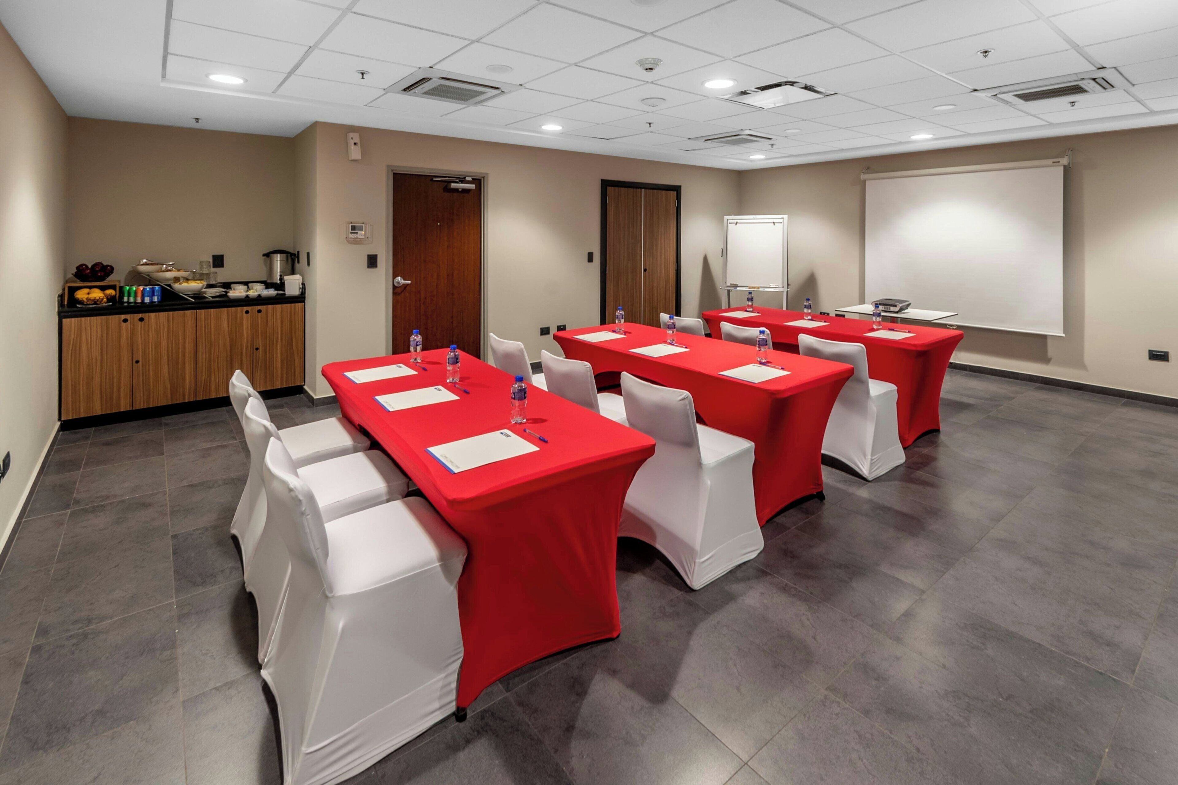 A conference room with red tables and white chairs, equipped with water bottles and notepads.