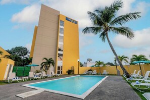 Un hotel con piscina, sillas de descanso y palmeras.