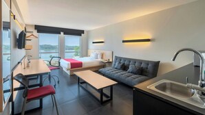 Una habitación de hotel moderna con cama, sofá, mesa de comedor y zona de cocina.