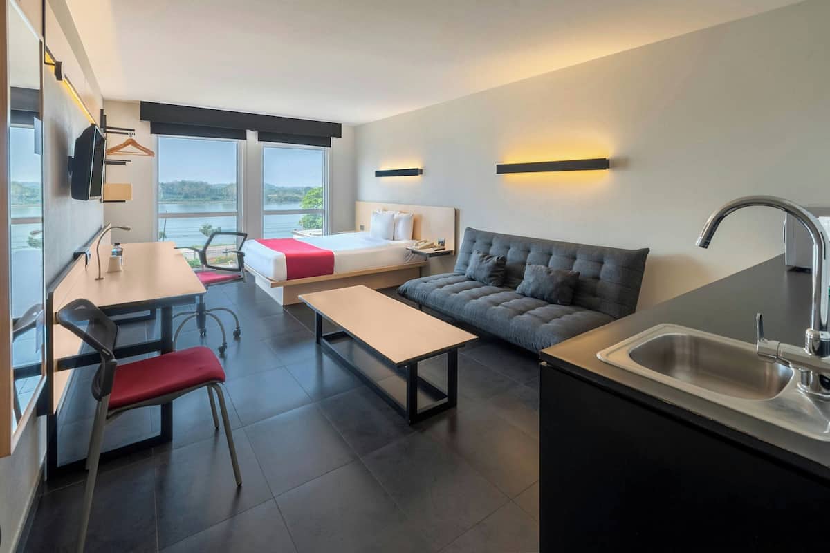 Ett modernt hotellrum med en säng, en soffa, ett matbord och ett litet kök.