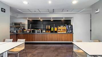 A modern kitchen with a wooden countertop, various appliances, and a coffee machine. There are two white tables with chairs in the foreground.