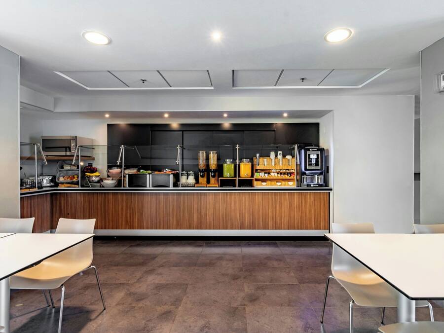 A modern kitchen with a wooden countertop, various appliances, and a coffee machine. There are two white tables with chairs in the foreground.