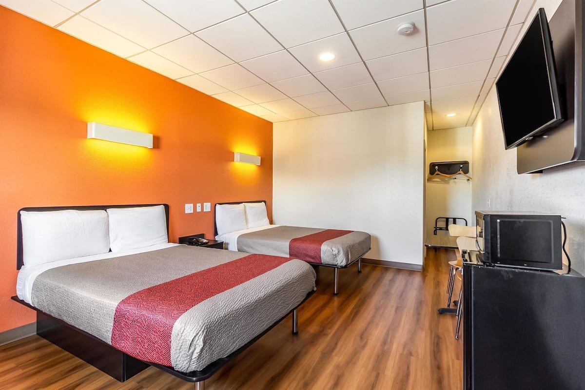 A hotel room with two beds, a TV, and a desk with a chair.