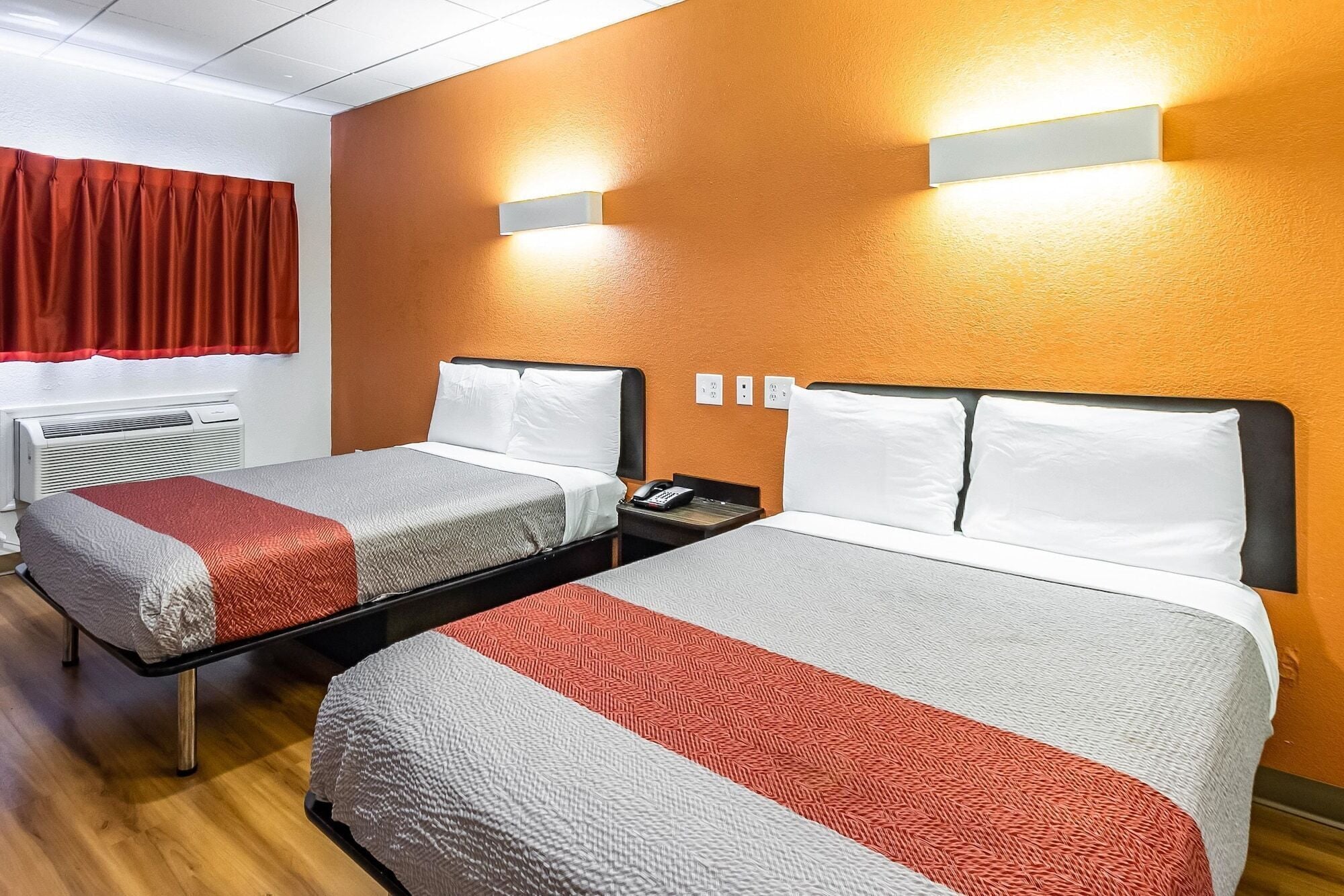 Ein Hotelzimmer mit zwei Betten, jeweils mit einer roten und weißen Bettdecke, einem Nachttisch mit Telefon sowie einer wandmontierten Lampe.