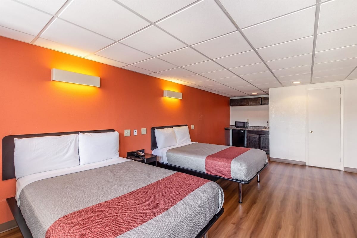 A hotel room with two beds, a kitchenette, and a bathroom.