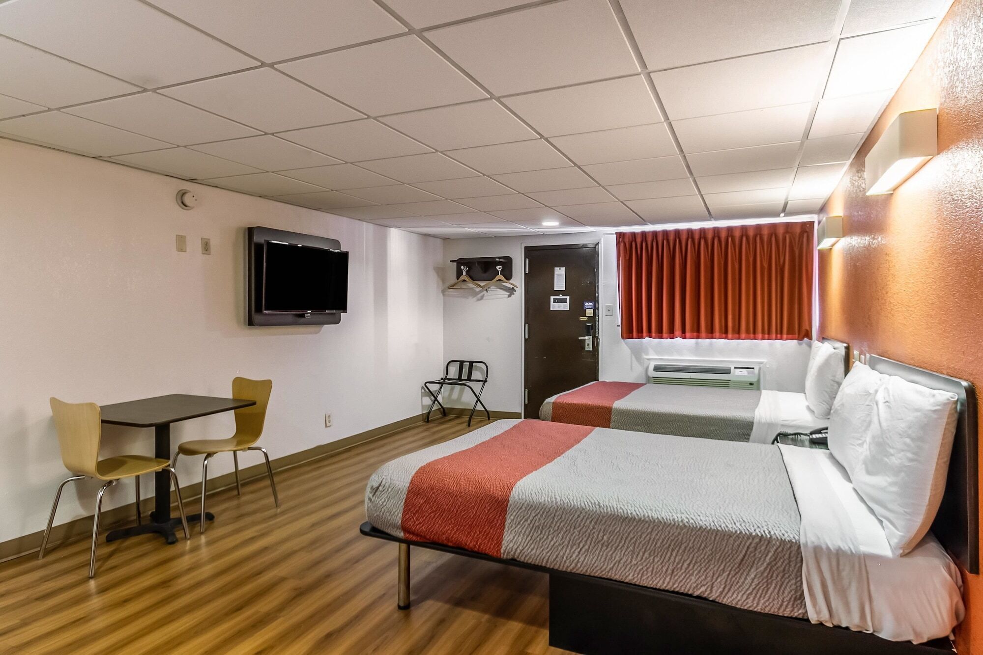 Habitación de hotel con dos camas, un televisor montado en la pared, un escritorio con una silla y una ventana con cortinas.