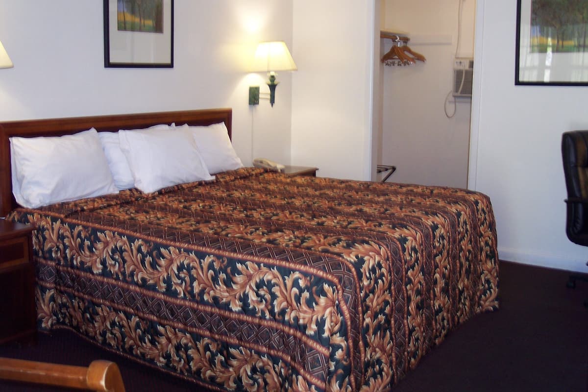 A neatly made bed with a patterned bedspread, a bedside lamp, and a framed picture on the wall.