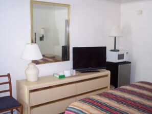 Habitación de hotel con cama, televisión, escritorio con lámpara, espejo y microondas.