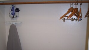 A room with a wooden ironing board, a hanging rack with wooden hangers, and a wall-mounted iron. - Shore Hills Motel (Manasquan)
