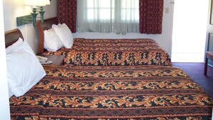 A double bed with a patterned bedspread, a bedside lamp, and a window with curtains. - Shore Hills Motel (Manasquan)