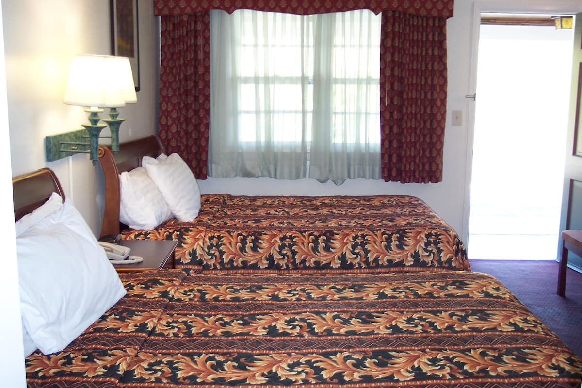 A double bed with a patterned bedspread, a bedside lamp, and a window with curtains.