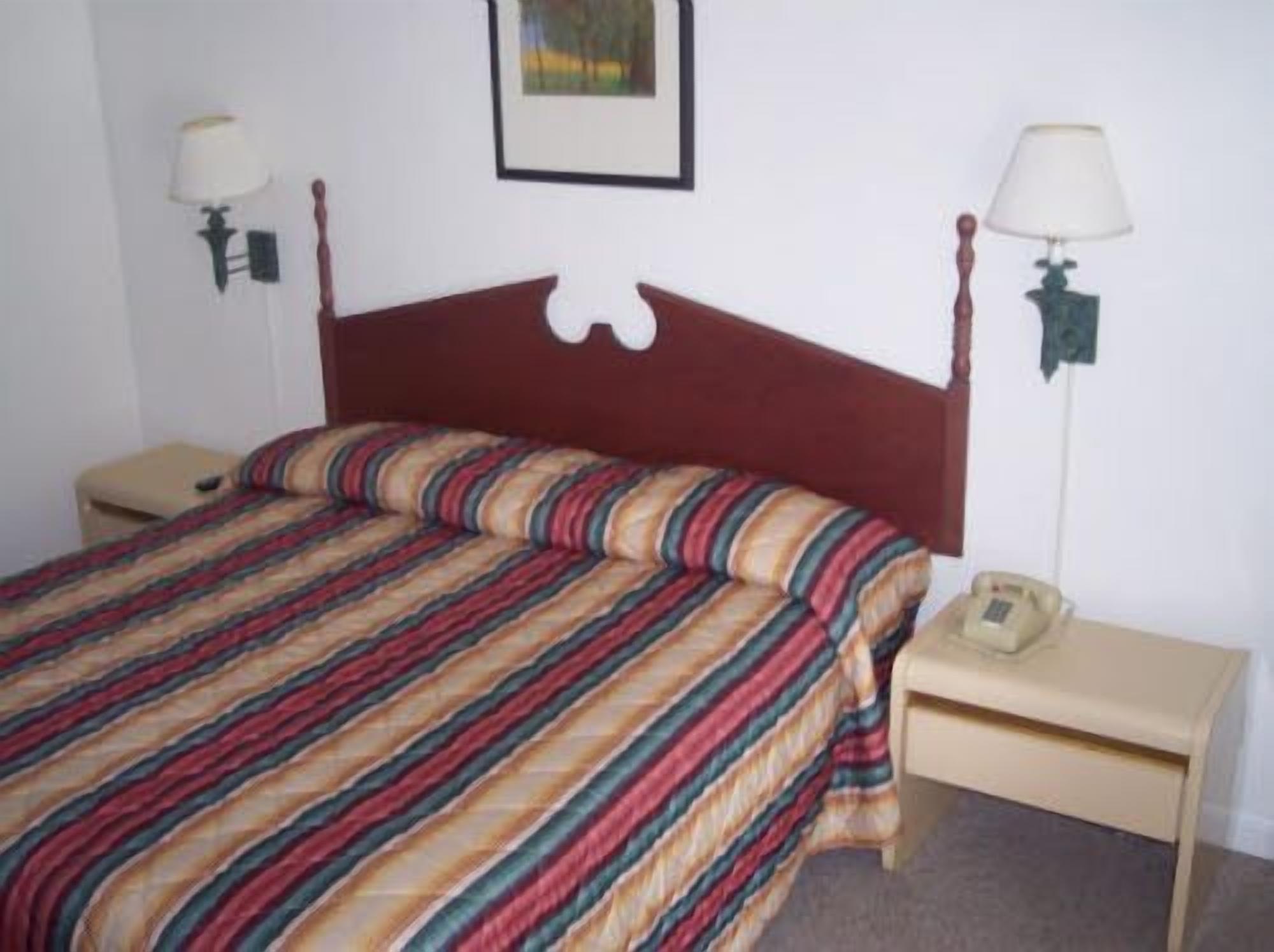 A single bed with a striped bedspread, two bedside tables with lamps, and a framed picture on the wall.