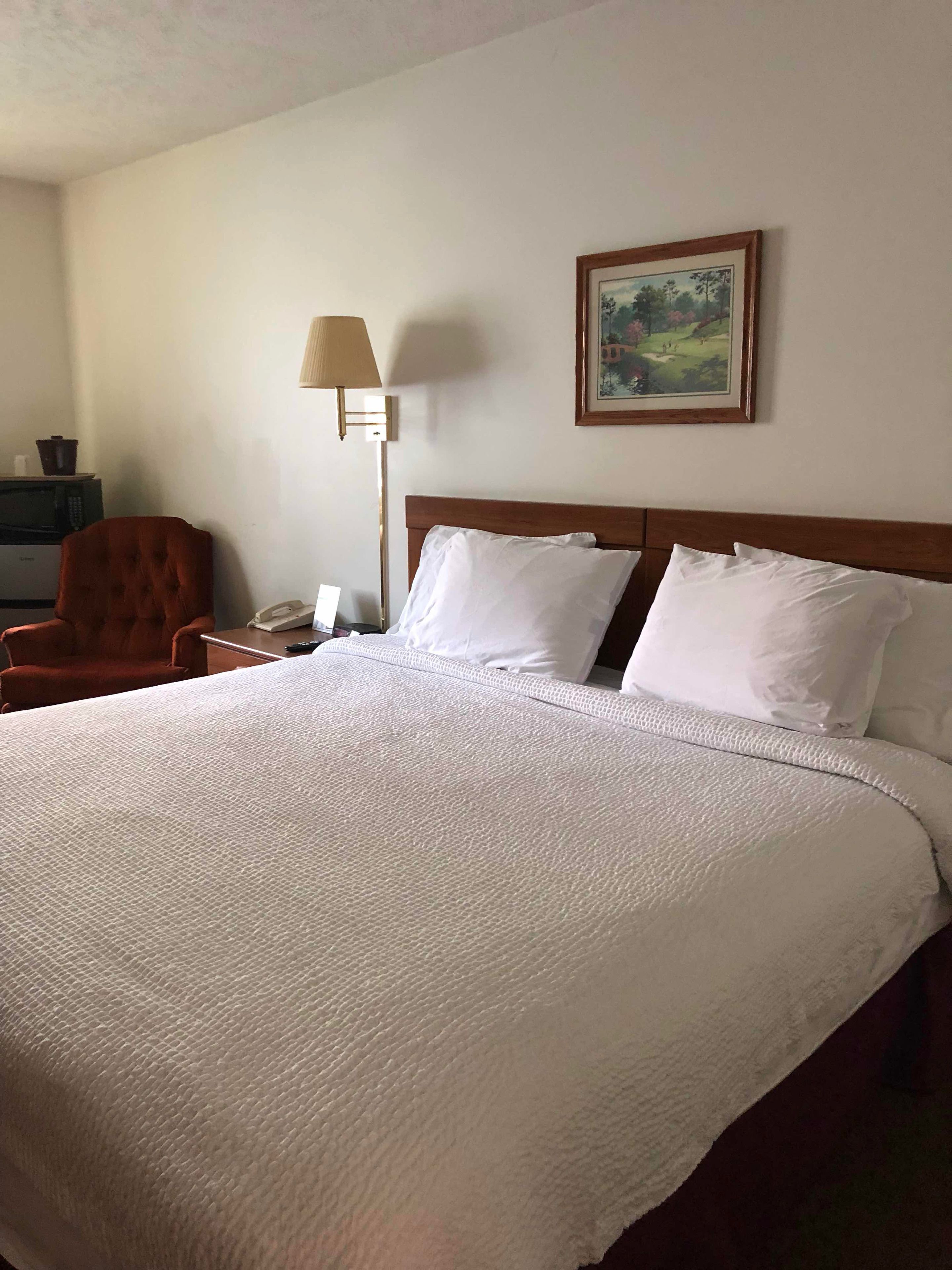 Een net opgemaakt bed met witte lakens, een houten hoofdbord en een enkele bedlamp.