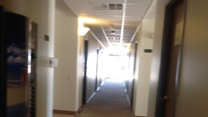 A corridor with doors on both sides, a carpeted floor, and a ceiling with recessed lighting. - Coronado Motel and RV Park (Lindsborg)