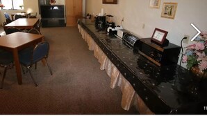 A kitchen with a long counter, a dining table with chairs, a refrigerator, and a cabinet. - Coronado Motel and RV Park (Lindsborg)