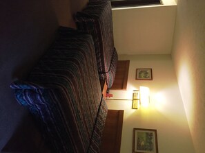 Quarto com uma cama, luminária na parede e duas quadros.