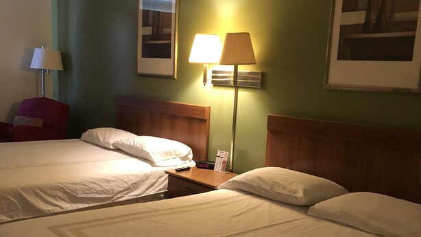 A hotel room with two beds, a nightstand, a lamp, and a chair. - Coronado Motel and RV Park (Lindsborg)