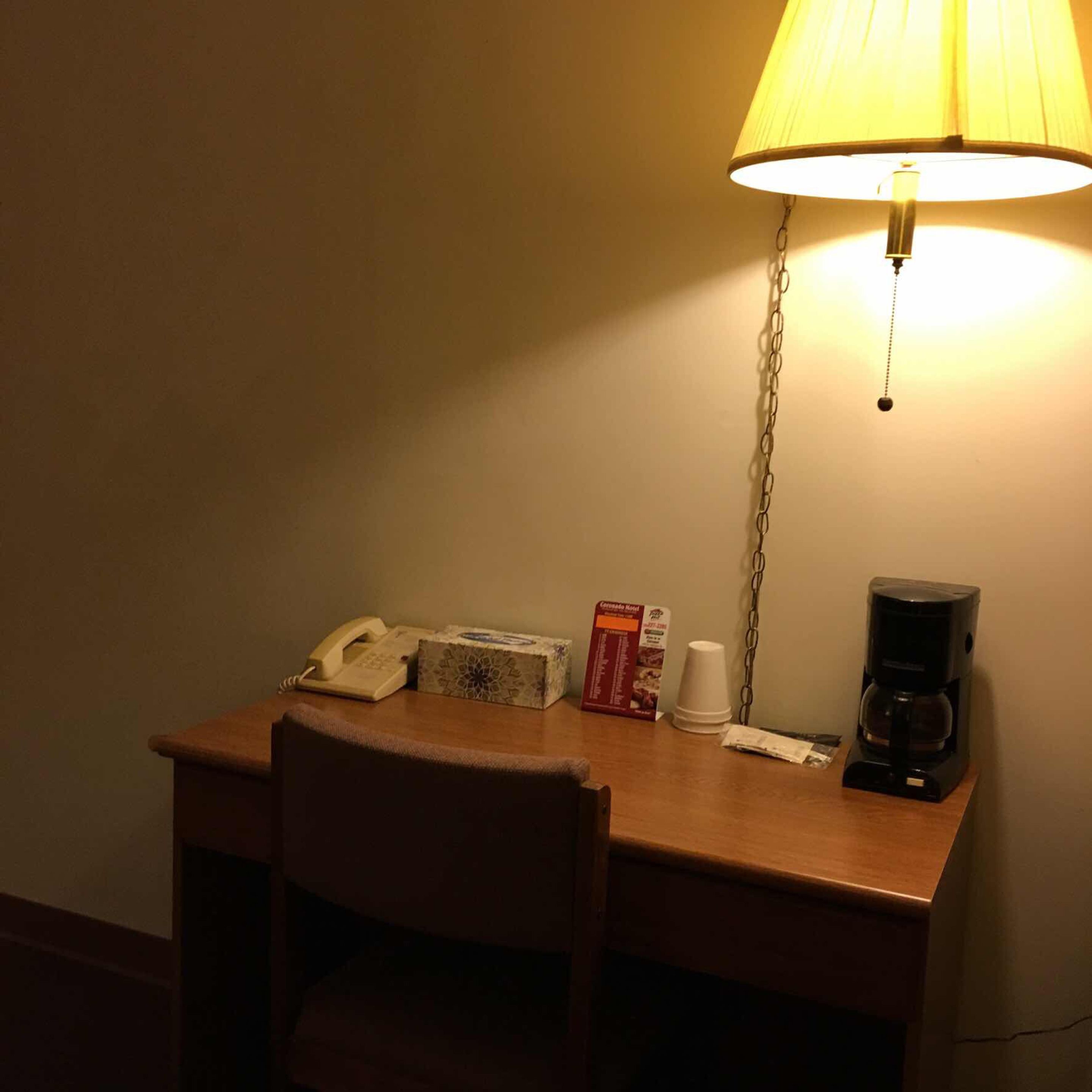 Escritorio de habitación de hotel con una lámpara, un teléfono, una cafetera y una caja de pañuelos.