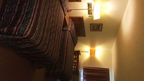 A room with a patterned bedspread, a wooden headboard, a wall-mounted light fixture, and a framed picture. - Coronado Motel and RV Park (Lindsborg)