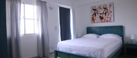 A bedroom with a bed, curtains, a painting, and a nightstand.