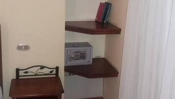 A corner room with a small wooden chair, a radio, and a shelf with books and a lamp.